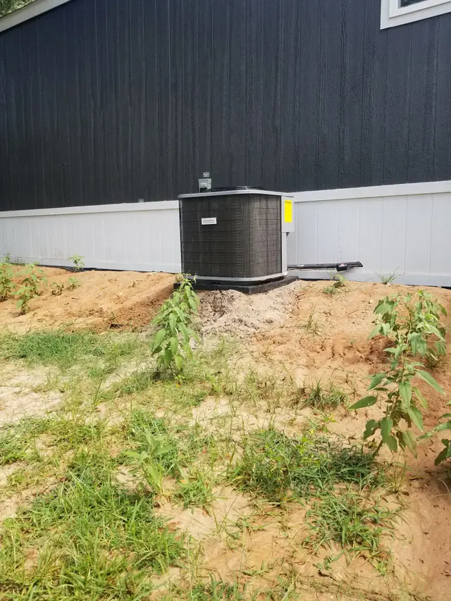 A GrandAire condenser set beside a navy manufactured home